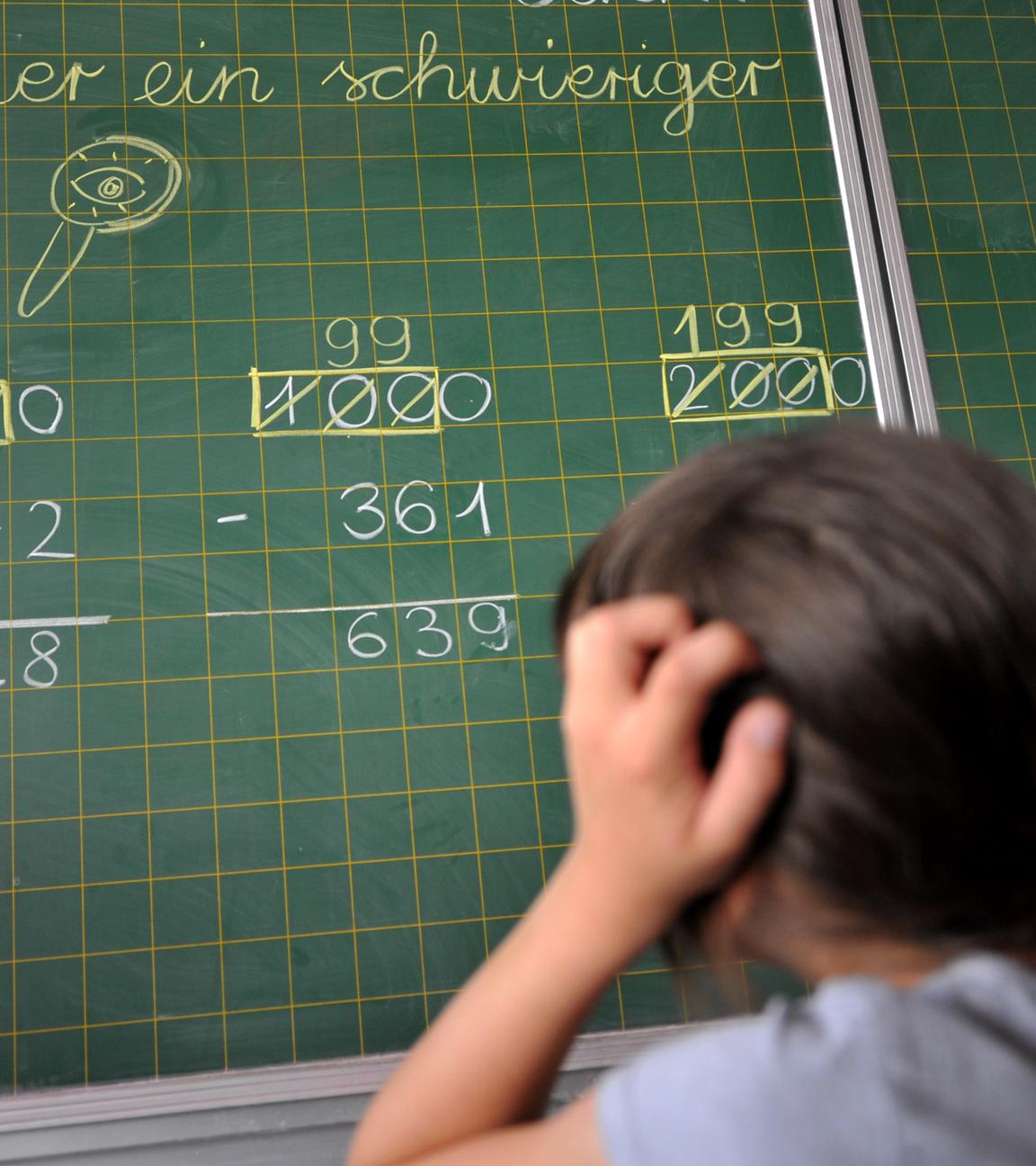 Ein Mädchen der zweiten Klasse der Grundschule steht an der Tafel vor einer Rechenaufgabe. 