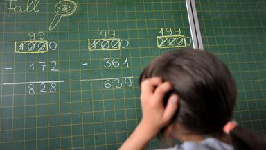 Ein Mädchen der zweiten Klasse der Grundschule steht an der Tafel vor einer Rechenaufgabe. 