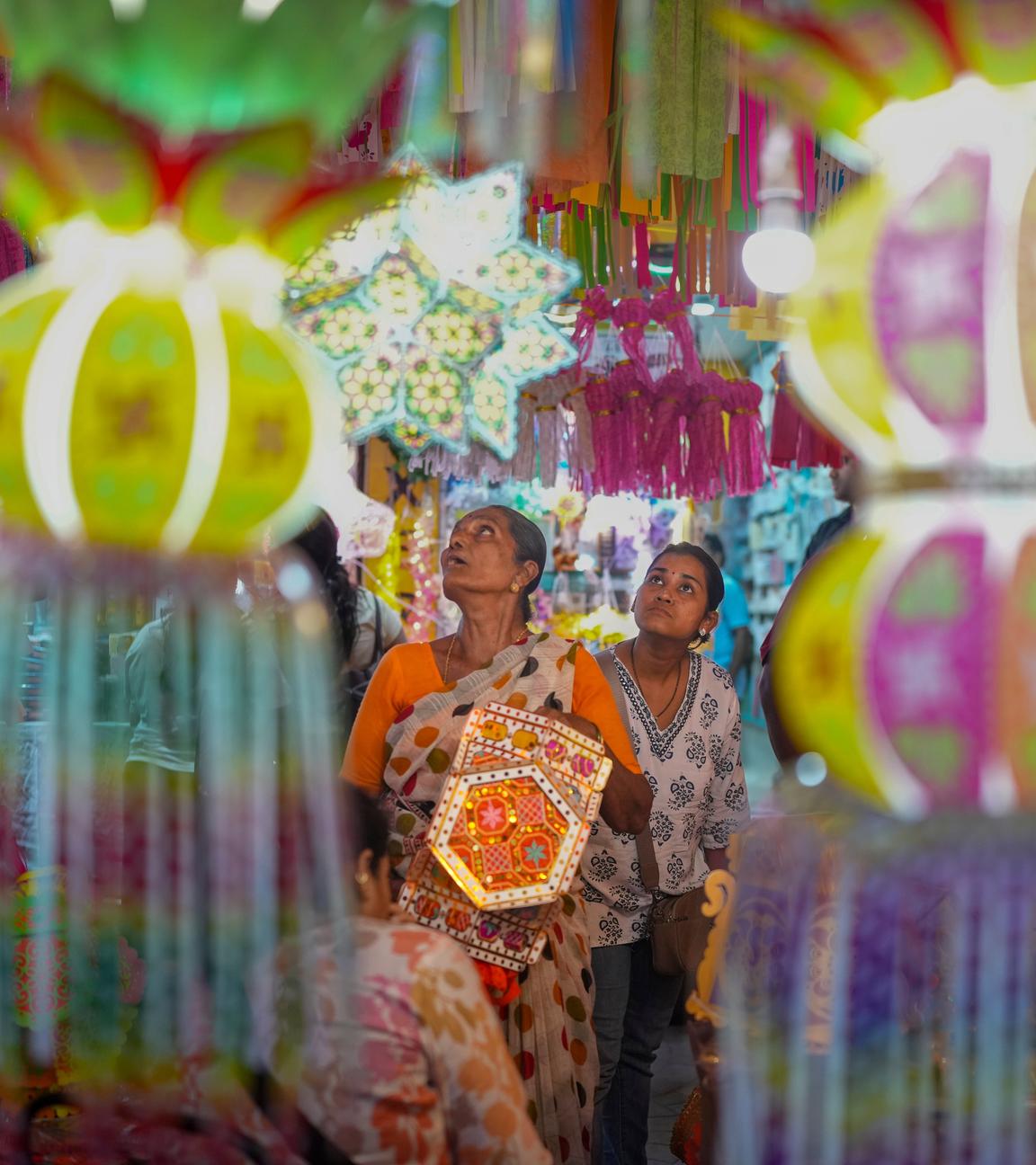 Auf dem Bild sind zwei Frauen in Indien zu sehen, die während die Diwali durch eine Straße laufen. Es ist sehr beschmückt und sehr farbenfroh.