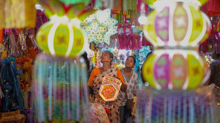 Auf dem Bild sind zwei Frauen in Indien zu sehen, die während die Diwali durch eine Straße laufen. Es ist sehr beschmückt und sehr farbenfroh.