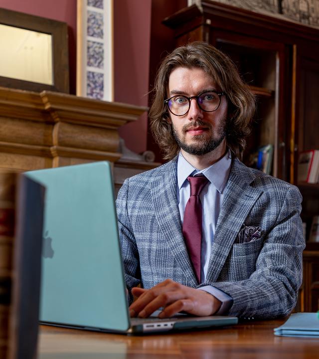Eryk Jan Grzeszkowiak in einer Bibliothek vor einem Laptop sitzend und in die Kamera schauend.