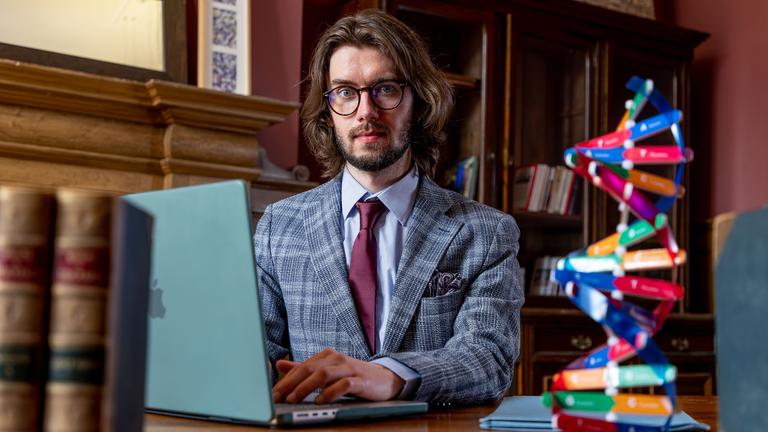 Eryk Jan Grzeszkowiak in einer Bibliothek vor einem Laptop sitzend und in die Kamera schauend.