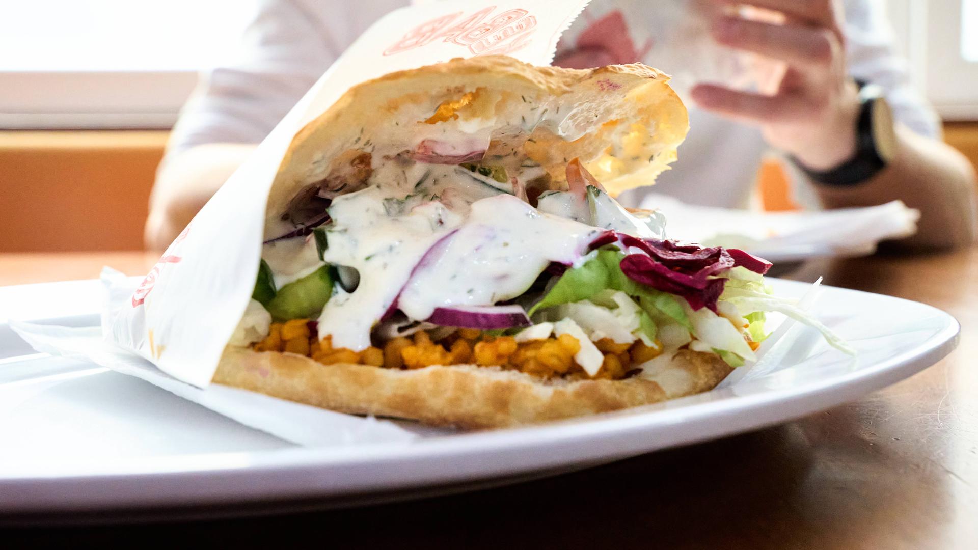 Auf einem weißen Teller ein Döner im Fladenbrot: mit Rotkraut, weißer Soße und Salat.