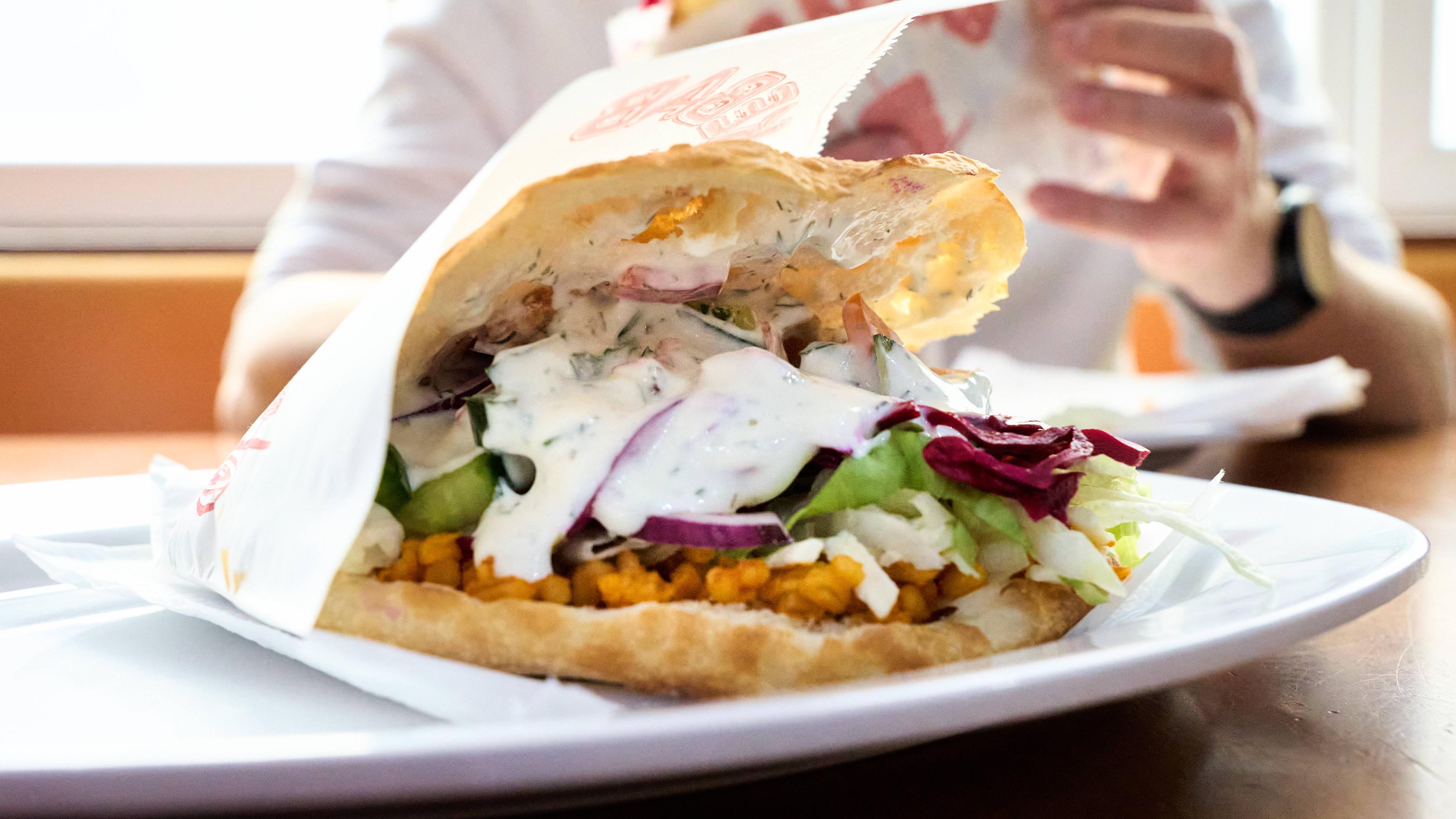 Auf einem weißen Teller ein Döner im Fladenbrot: mit Rotkraut, weißer Soße und Salat.