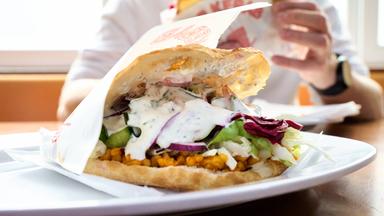 Auf einem weißen Teller ein Döner im Fladenbrot: mit Rotkraut, weißer Soße und Salat.