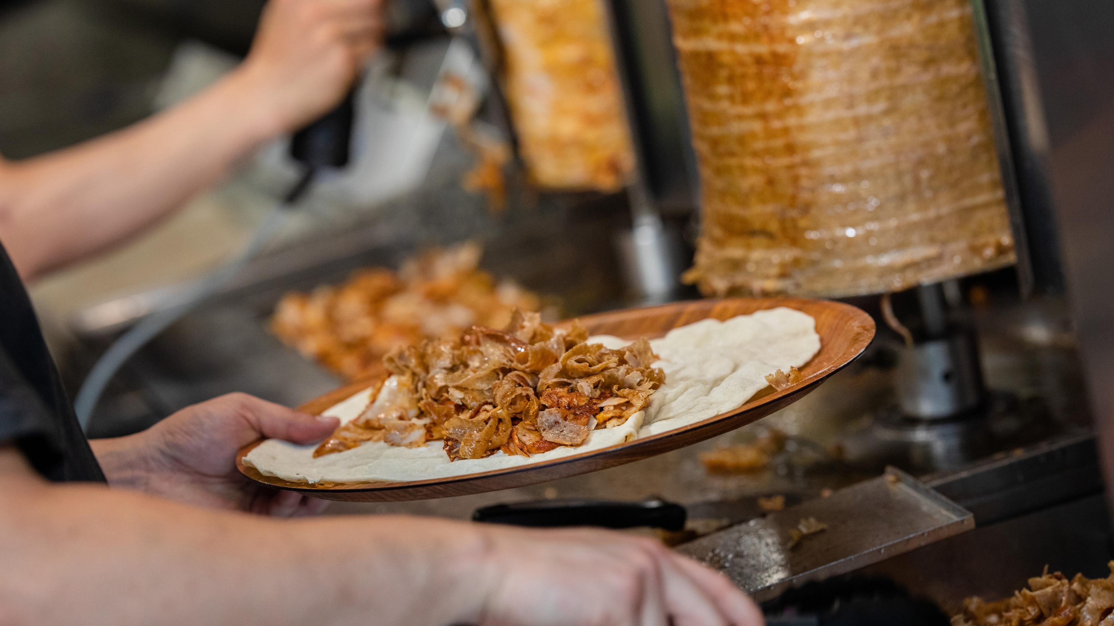  Ein Mitarbeiter einer Dönerbude legt Fleisch auf einen Döner.