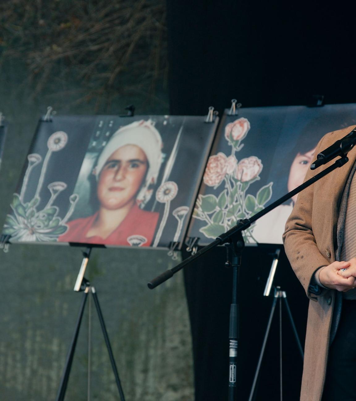 Ein Mann, der einen braunen Mantel trägt, steht rechts von drei Gedächtnisfotografien, die drei Frauen zeigen.