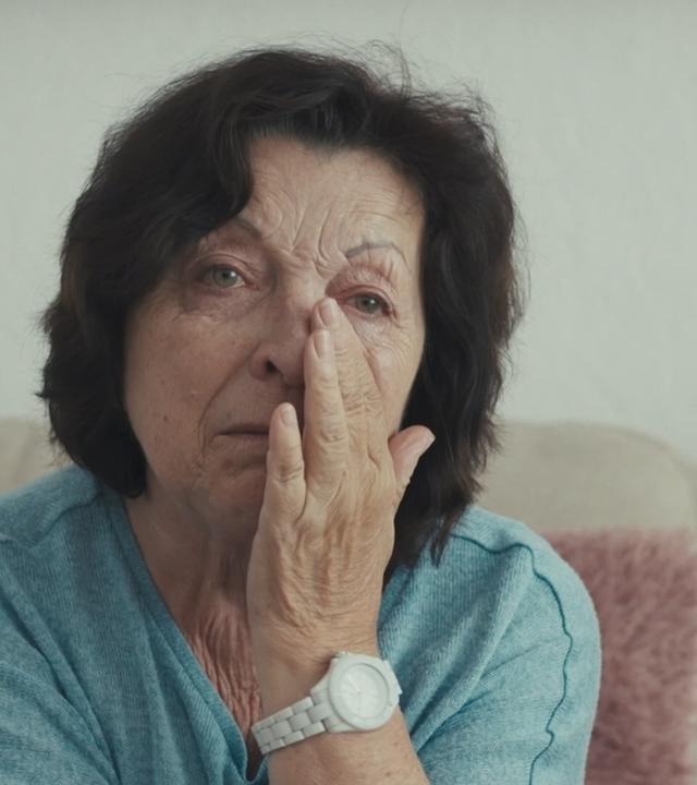 Eine Frau hält die Hand unter den Augen, kämpft mit Tränen.