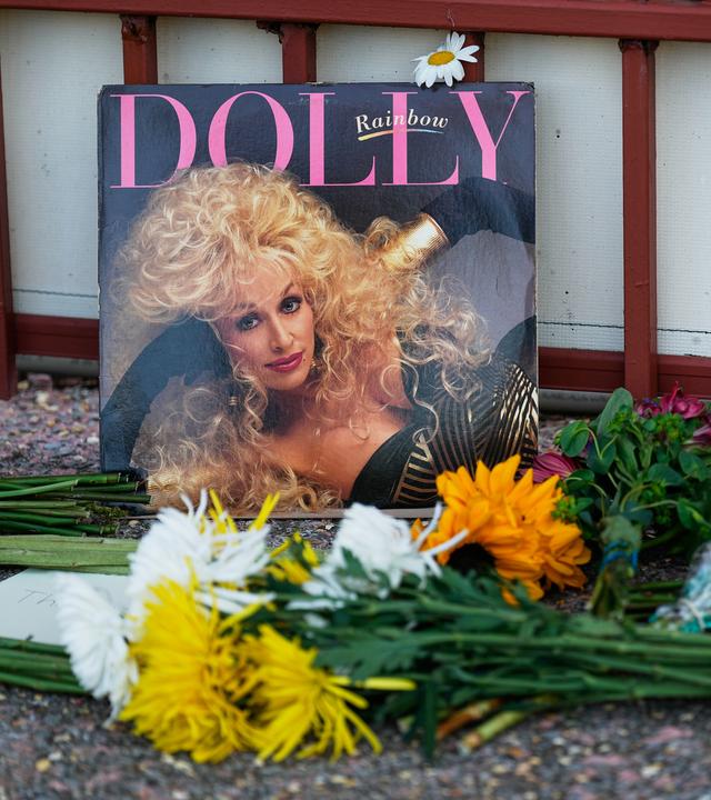 Eine Platte von Dolly Parton ist an ein Gebäude angelehnt, davor wurden Blumen niedergelegt