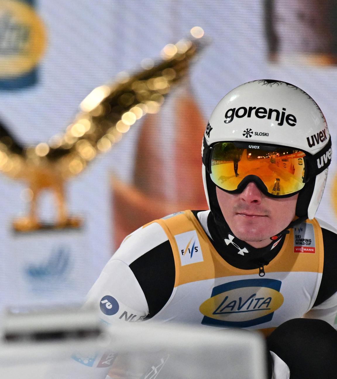 Domen Prevc in der Hocke vor dem Pokal der Vierschanzentournee