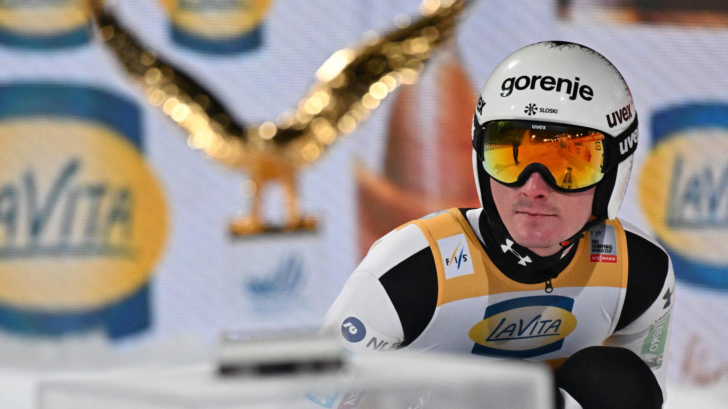 Domen Prevc in der Hocke vor dem Pokal der Vierschanzentournee