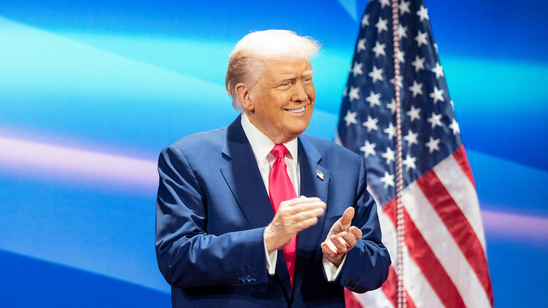 Donald Trump klatschend, Amerikafahne im Hintergrund