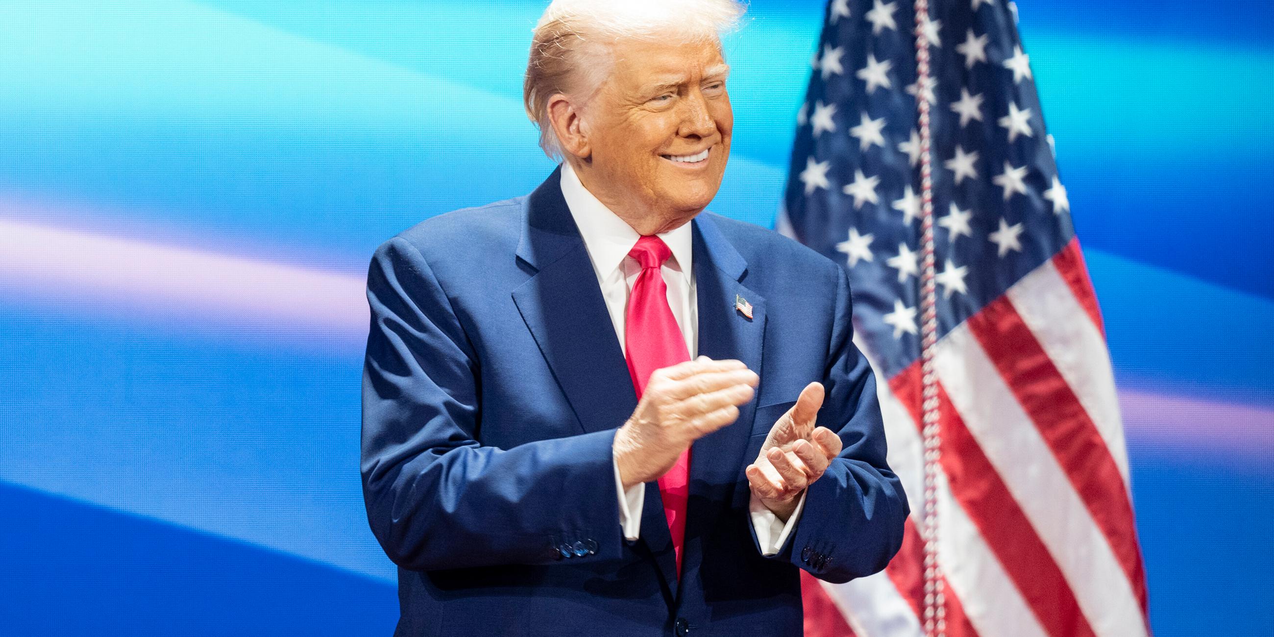 Donald Trump klatschend, Amerikafahne im Hintergrund