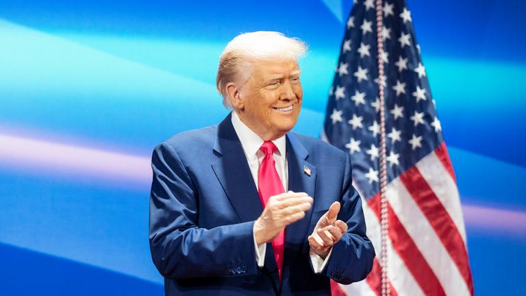 Donald Trump klatschend, Amerikafahne im Hintergrund