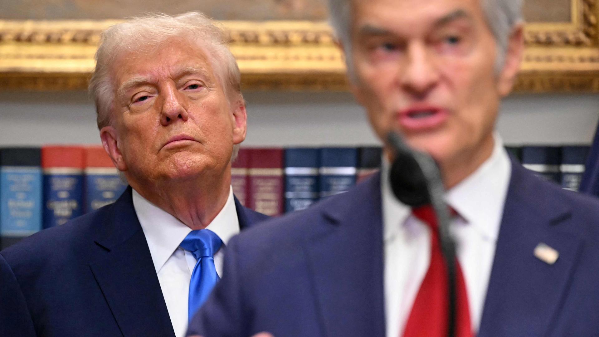 Donald Trump schaut kritisch aus dem Hintergrund zu Mehmet Oz