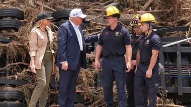 Donald und Melania Trump im Gespräch mit Ersthelfern bei der Flut, im Hintergrund ein Haufen aus Reifen und Ästen