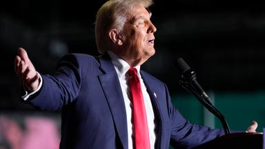 Donald Trump steht mit weit ausgestrckten Armen inter einen Rednerpult und schaut ins Publikum.