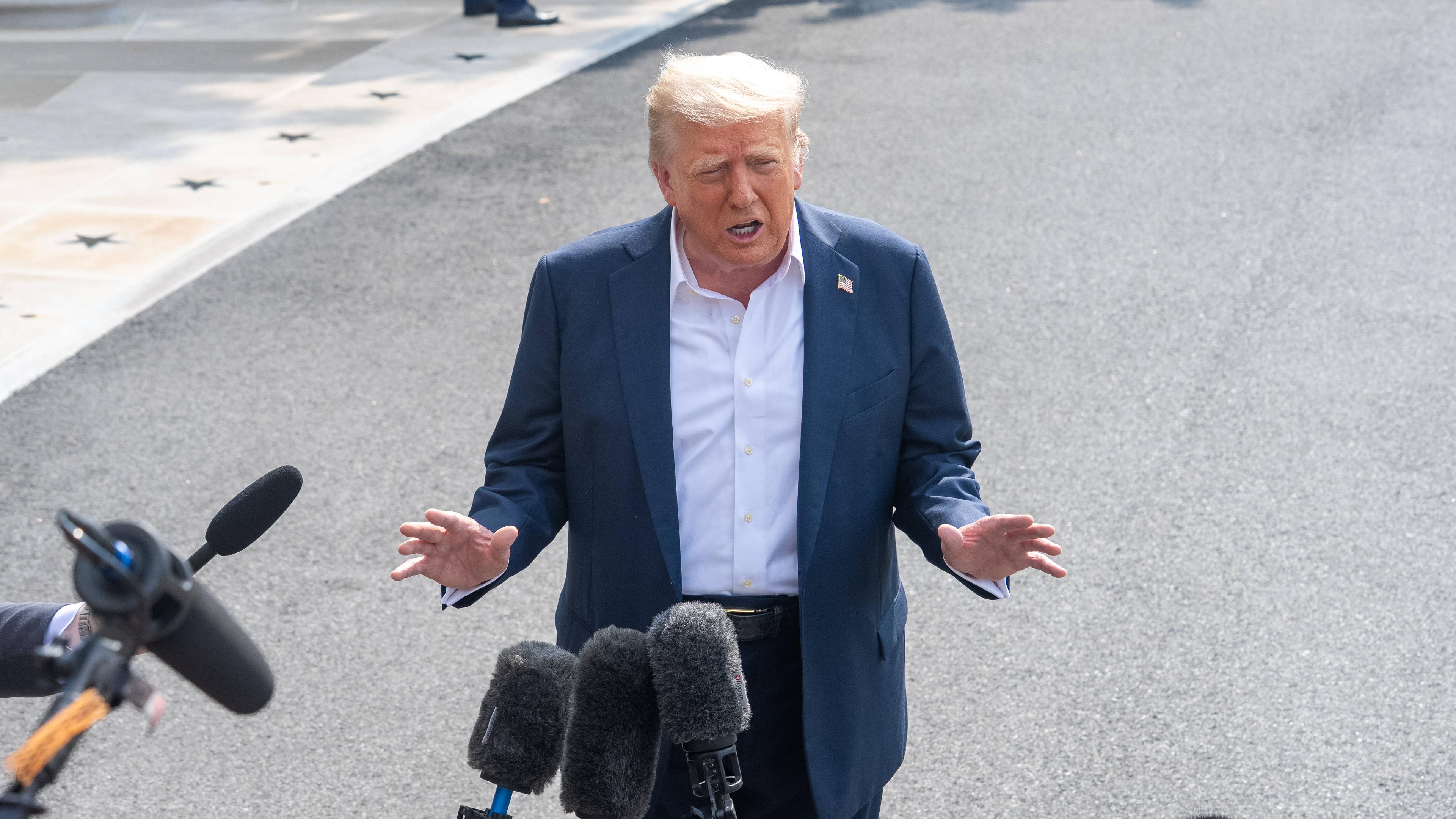 Donald Trump steht vor zahlreichen Mikrofonen und spricht mit Reportern, die nicht zu sehen sind.