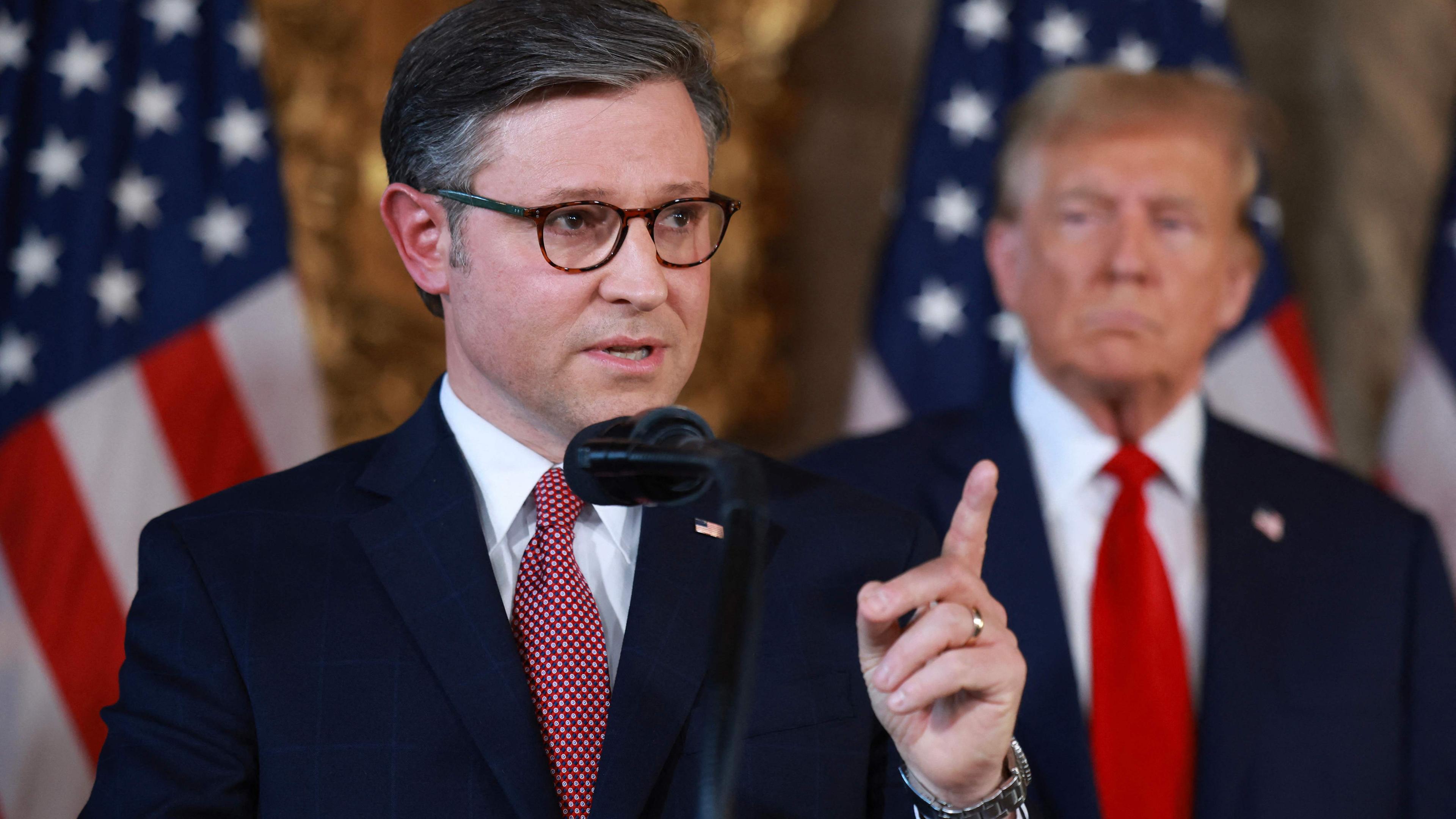 Mike Johnson, Sprecher des Repräsentantenhauses, hält eine Rede. Im Hintergrund steht Ex-Präsident Donald Trump.