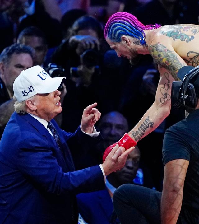 US-Präsident Donald Trump, ein älterer Mann mit Baseball-Kappe und im dunkelblauen Anzug gibt einem MMA-Kämpfer mit nacktem tätowierten Oberkörper und gefärbten Haaren die Hand, während er mit dem Finger auf ihn zeigt und redet.