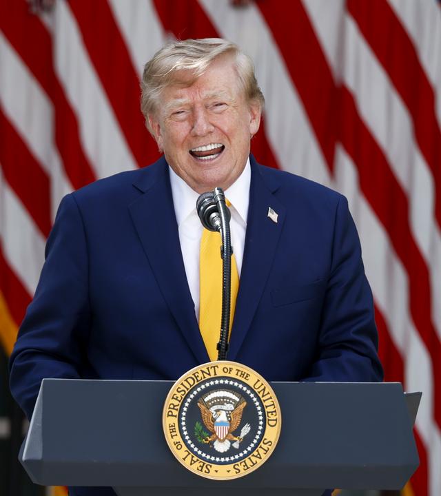 Donald Trump steht an einem Rednerpult und lacht.