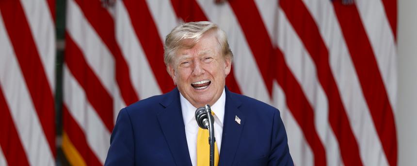 Donald Trump steht an einem Rednerpult und lacht.