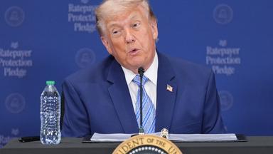 Donald Trump sitzt an einem Rednerpult und spricht in ein Mikrofon.