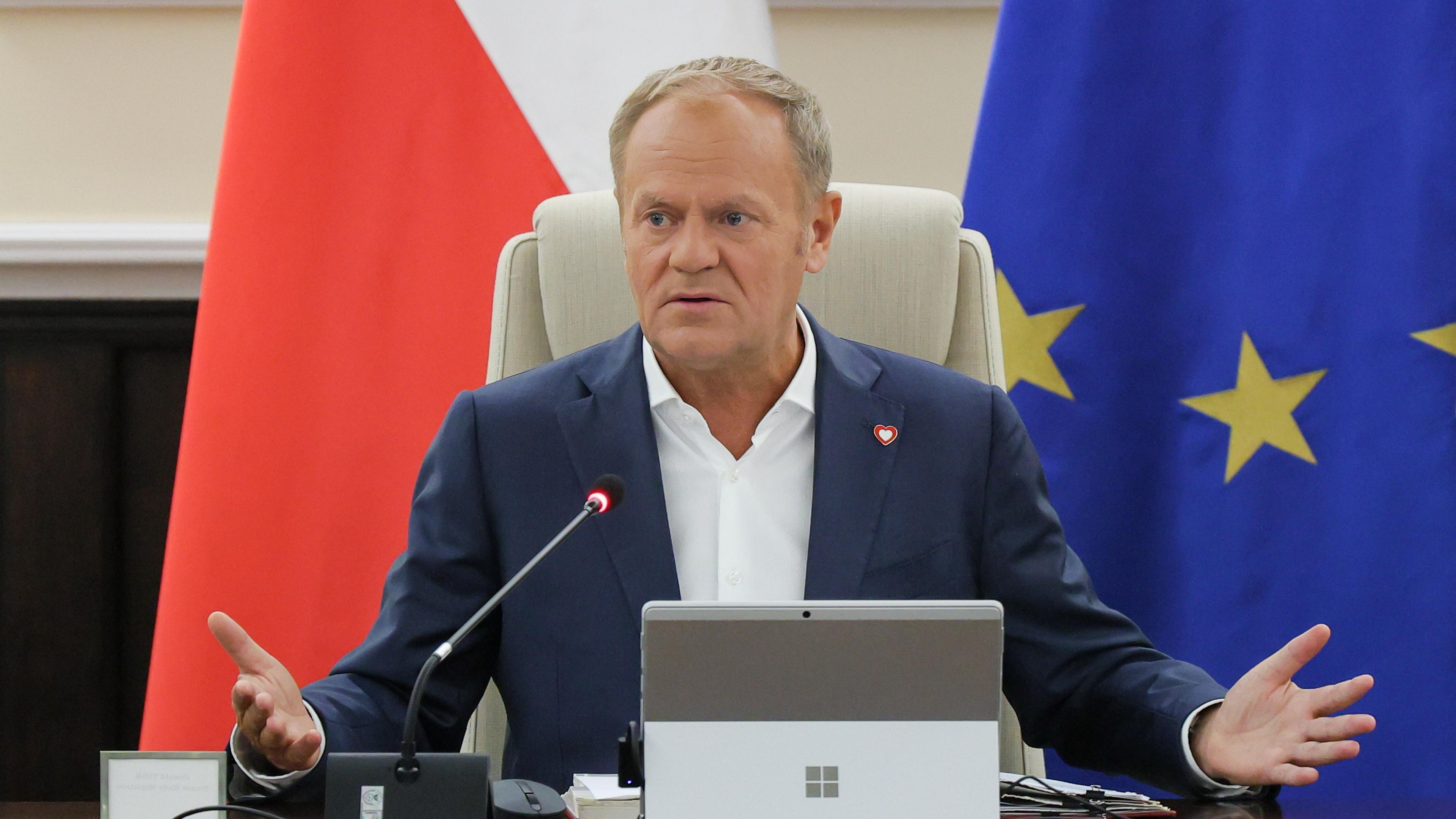Donald Tusk sitzend vor einer polnischen und einer EU-Fahne