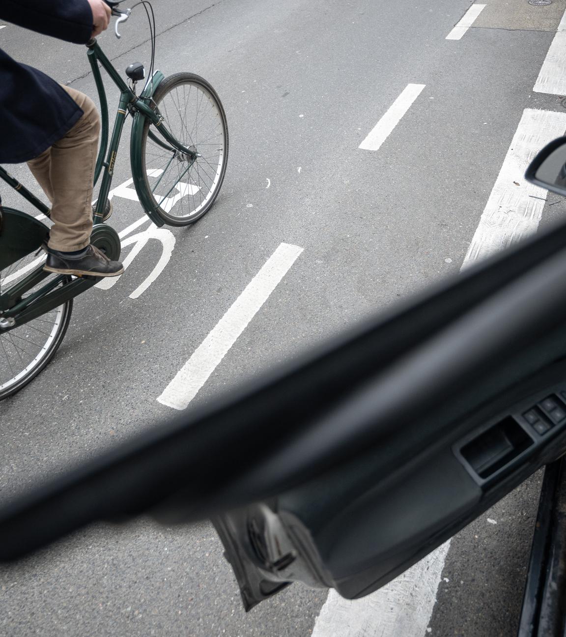 Symbolbild: Ein Fahrradfahrer fährt auf einer Fahrradstraße an einem Schutzstreifen für geöffnete Türen an Autos vorbei. 