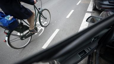 Symbolbild: Ein Fahrradfahrer fährt auf einer Fahrradstraße an einem Schutzstreifen für geöffnete Türen an Autos vorbei. 