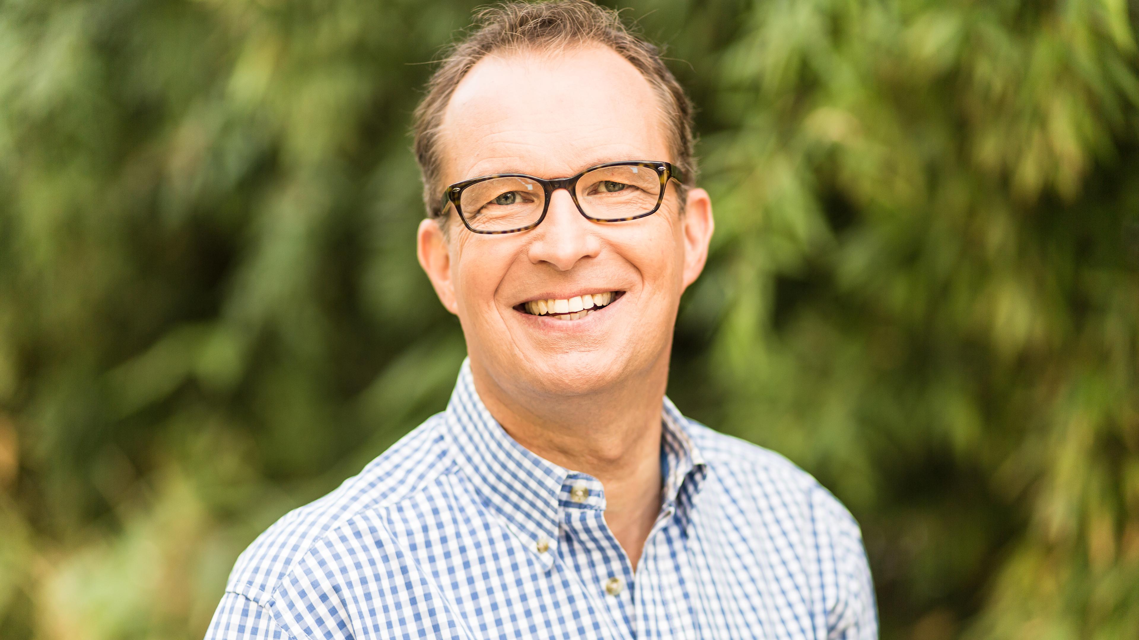 Dr. Christoph Specht steht mit kariertem Hemd vor dem unscharfen Hintergrund einiger Pflanzen.