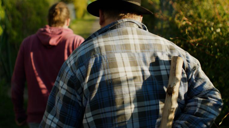 Ein Mann schleicht einem anderen Mann auf dem Gartenweg hinterher und verfolgt ihn.