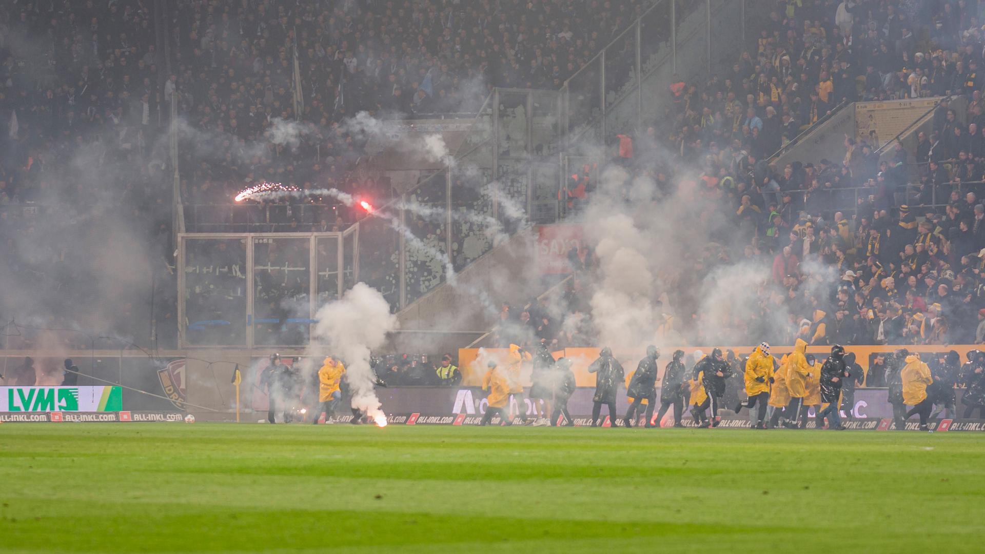 Während der Zweitligapartie zwischen Dynamo Dresden und Hertha BSC stürmen Dresdner Ultras den Platz und werfen Pyrotechnik in den Gästeblock der Berliner