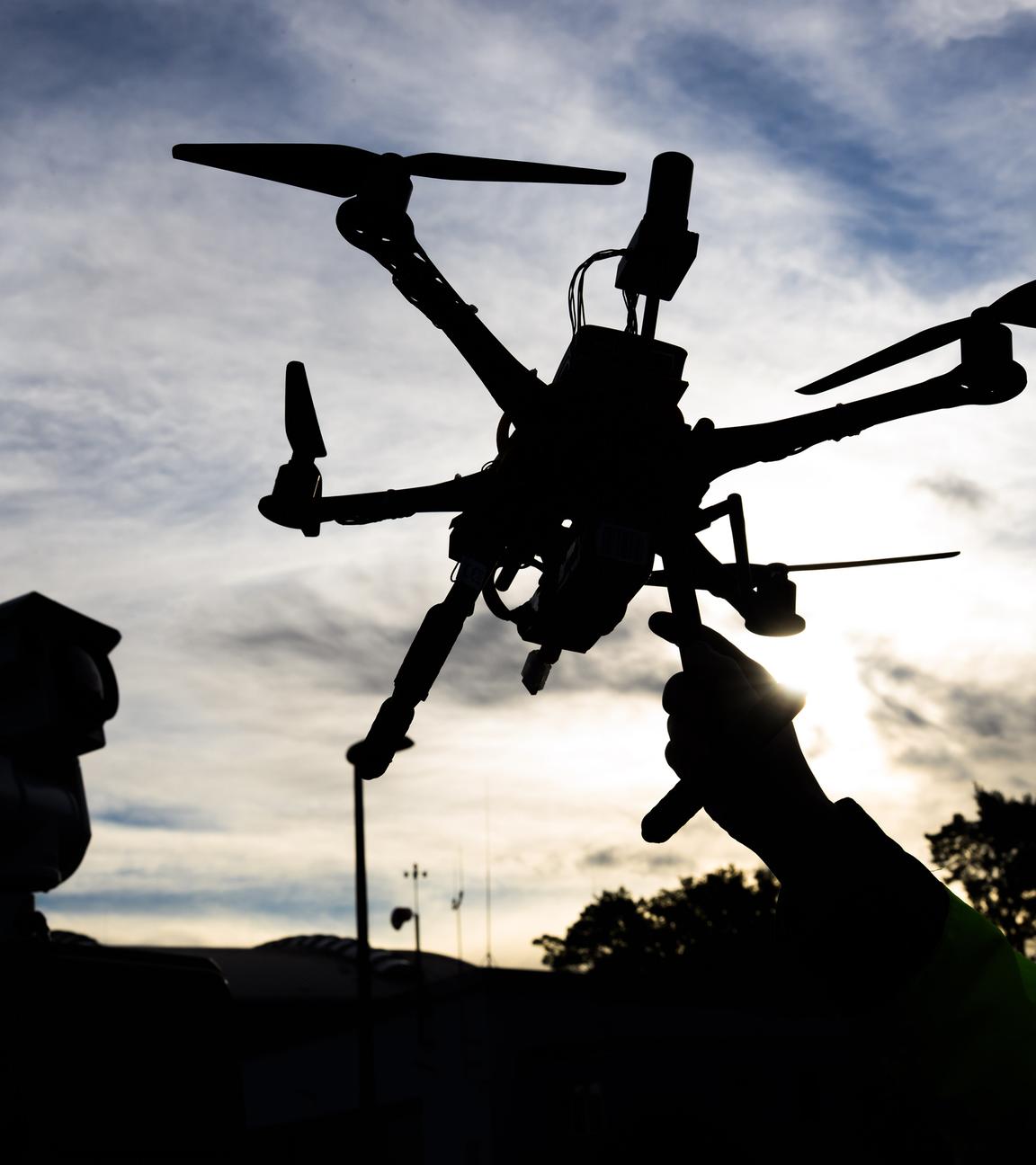 Der dunkle Umriss einer Drohne, die von einer Hand vor einen bewölkten Himmel hochgehalten wird.