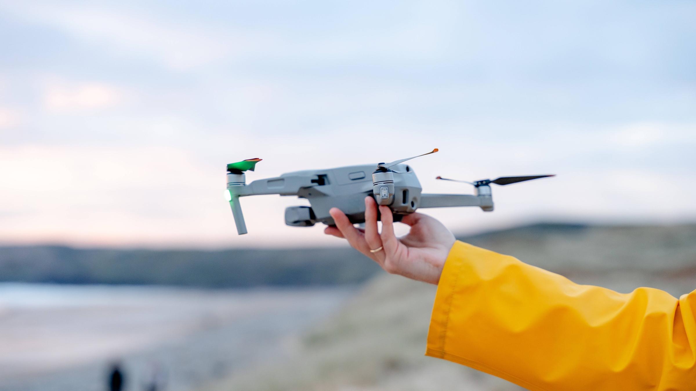 Eine Frau in einem gelben Regenmantel lässt an der Küste eine Drohne steigen.