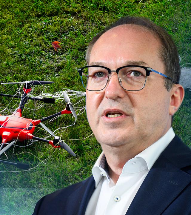 Innenminister Dobrindt vor einer Grafik mit einer kleinen Drohne auf einer Wiese liegend.