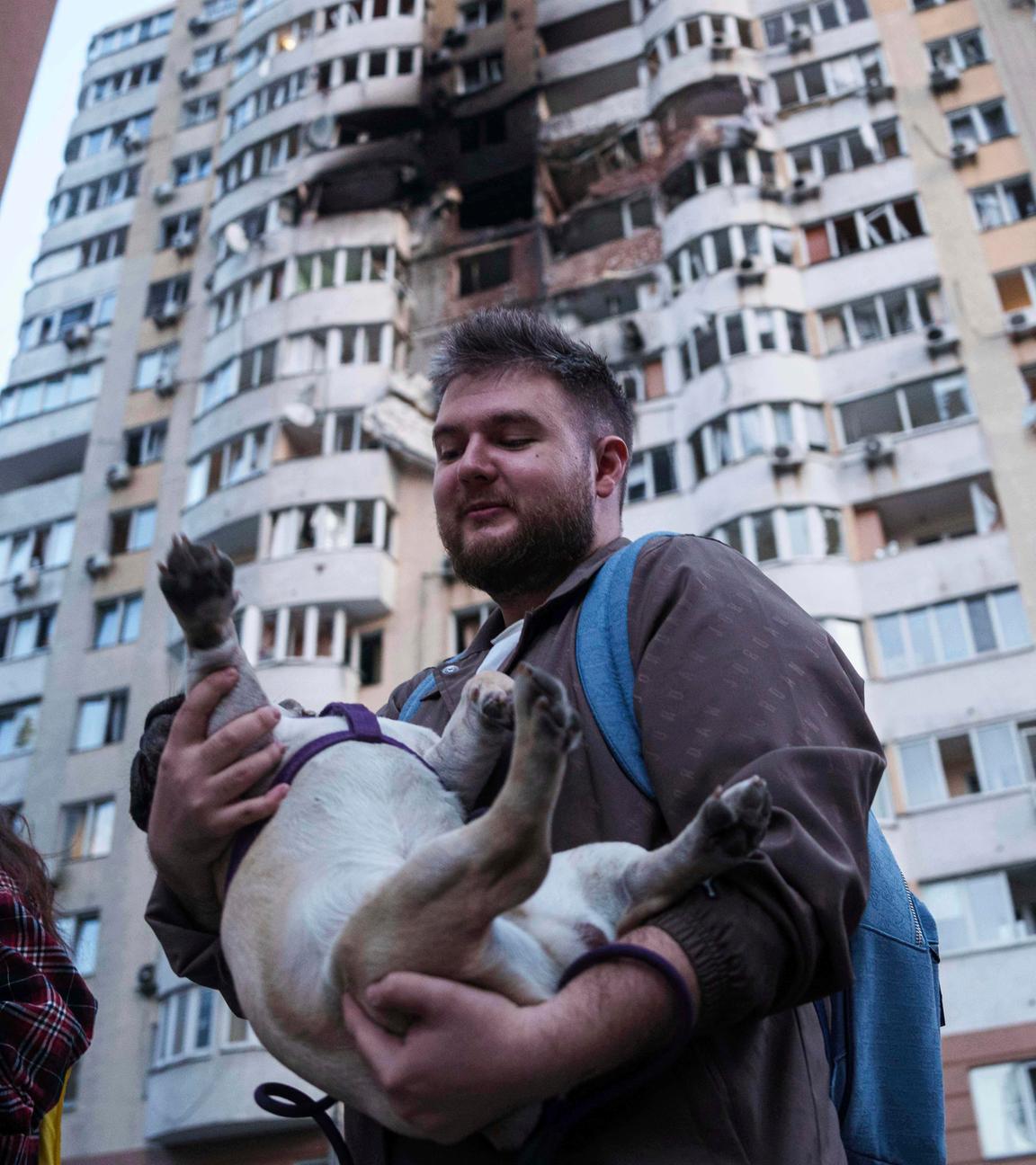Ein Mann trägt seinen Hund vor einem mehrstöckigen Wohnhaus, das bei einem russischen Drohnenangriff auf Kiew, Ukraine, beschädigt wurde. 