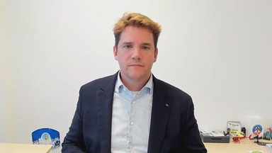 Daniel Sülberg vor einer weißen Wand. Er trägt Hemd und Sakko.