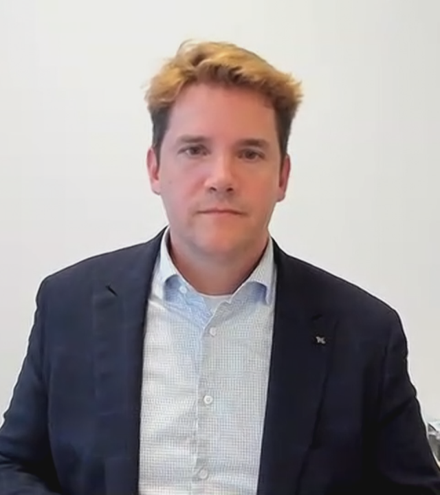 Daniel Sülberg vor einer weißen Wand. Er trägt Hemd und Sakko.