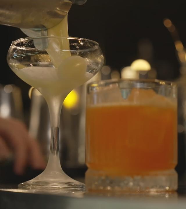 Zwei Cocktailgläser auf dem Tisch: In ein Glas wird noch ein Cocktail gefüllt