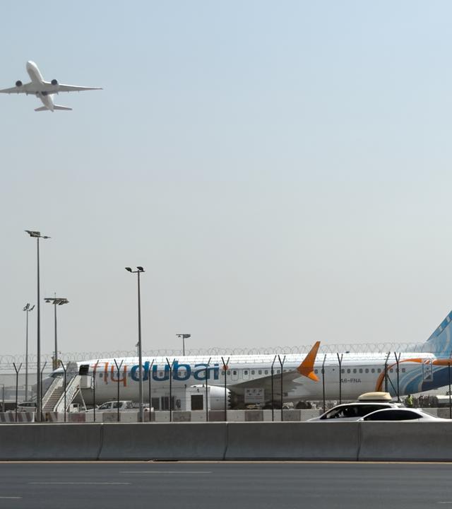 Ein Flugzeug hebt ab, während ein Flugzeug der Fluggesellschaft Flydubai auf dem Rollfeld des Dubai International Airport steht.