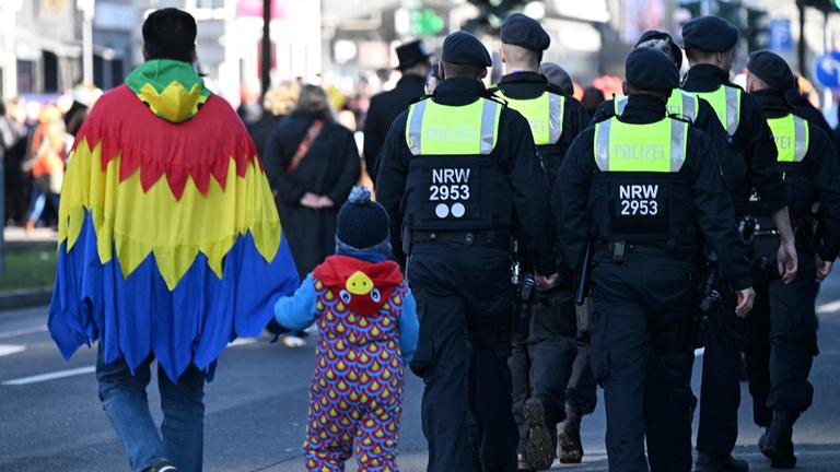 Kostümierte Zuschauer laufen während des Rosenmontagsumzugs hinter einer Gruppe von Polizeibeamten in Düsseldorf.