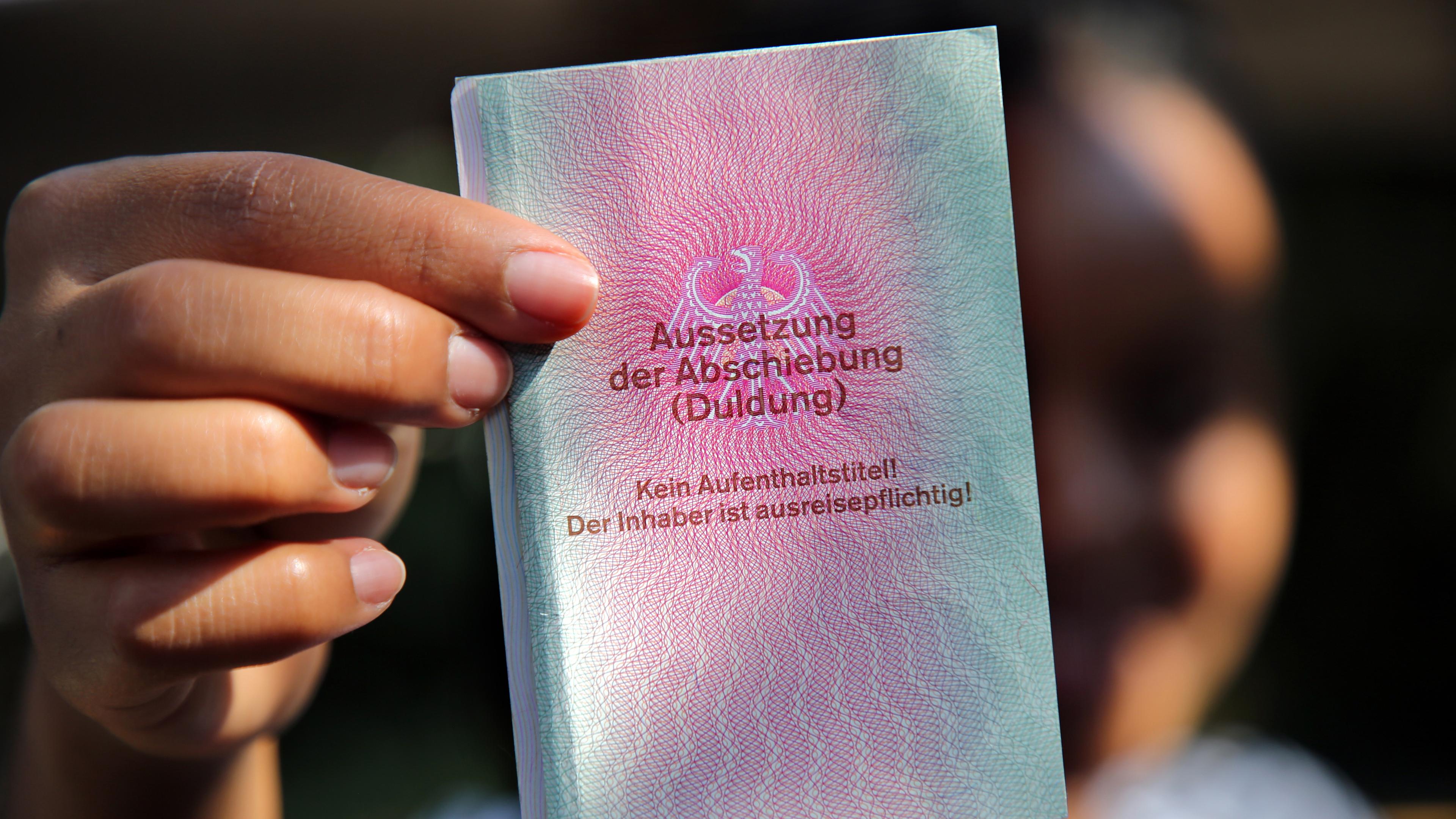 Eine junge Frau aus Afrika hält einen Ausweis für Flüchtlinge in der Hand mit dem Titel: Aussetzung der Abschiebung (Duldung)