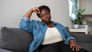 Dunkelhäutige Frau sitzt nachdenklich auf einem Sofa