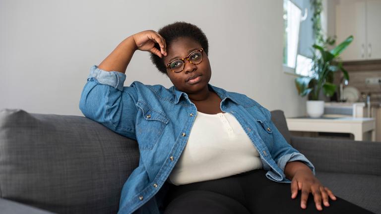 Dunkelhäutige Frau sitzt nachdenklich auf einem Sofa