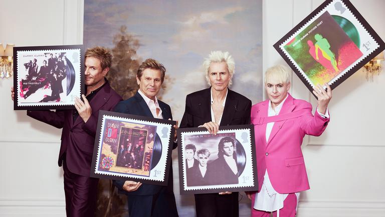 Die Band Duran Duran ist zu sehen, wie sie ihre eigenen Briefmarken hochhalten.