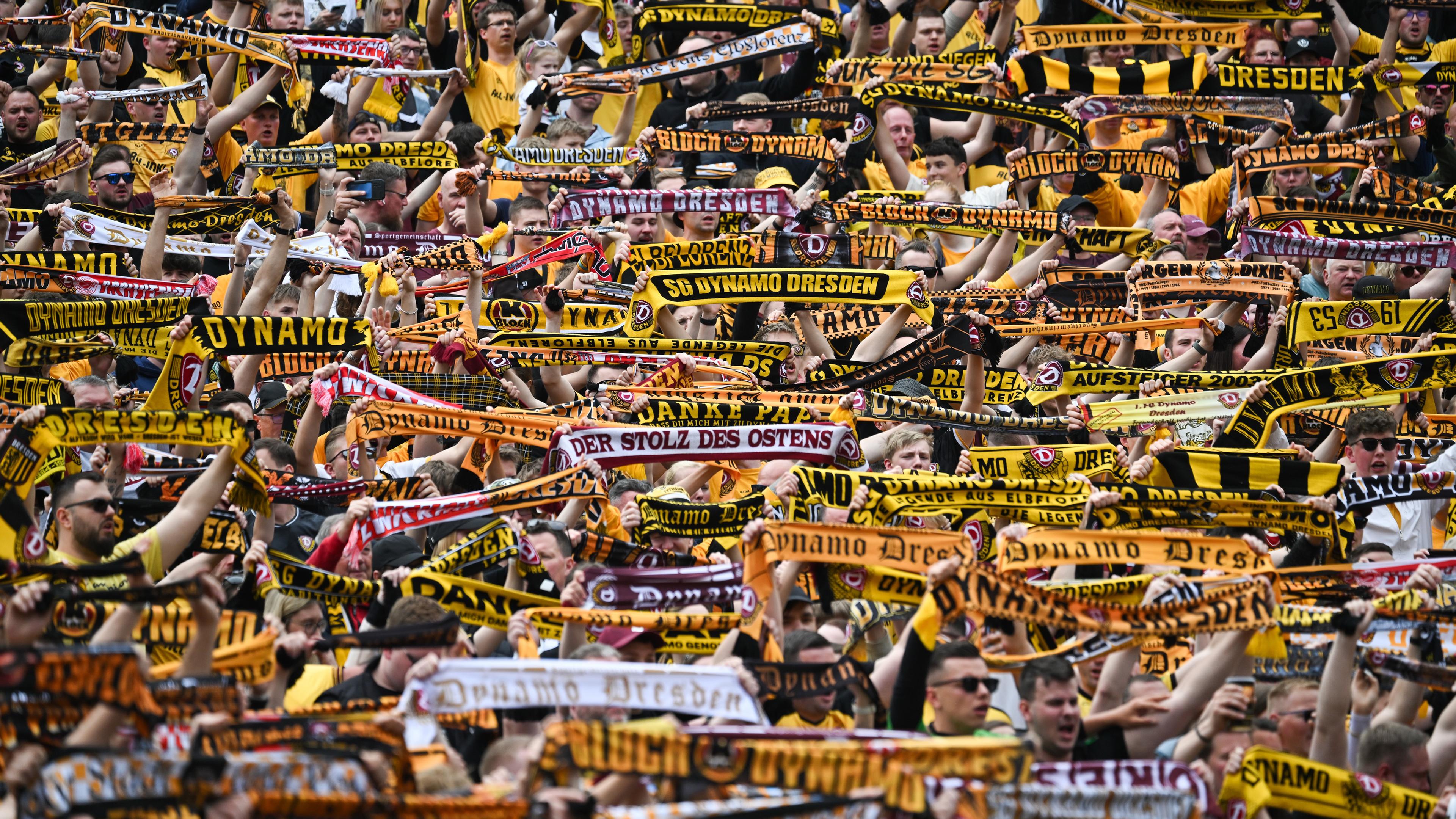 Dynamo Dresden Fans halten schwarz-gelbe Fan-Schals in die Höhe.