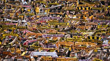 Dynamo Dresden Fans halten schwarz-gelbe Fan-Schals in die Höhe.