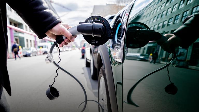 Ein Mann nimmt an einem Auto mit Plug-in-Hybrid-Antrieb in Berlin-Mitte den Ladestecker raus. 
