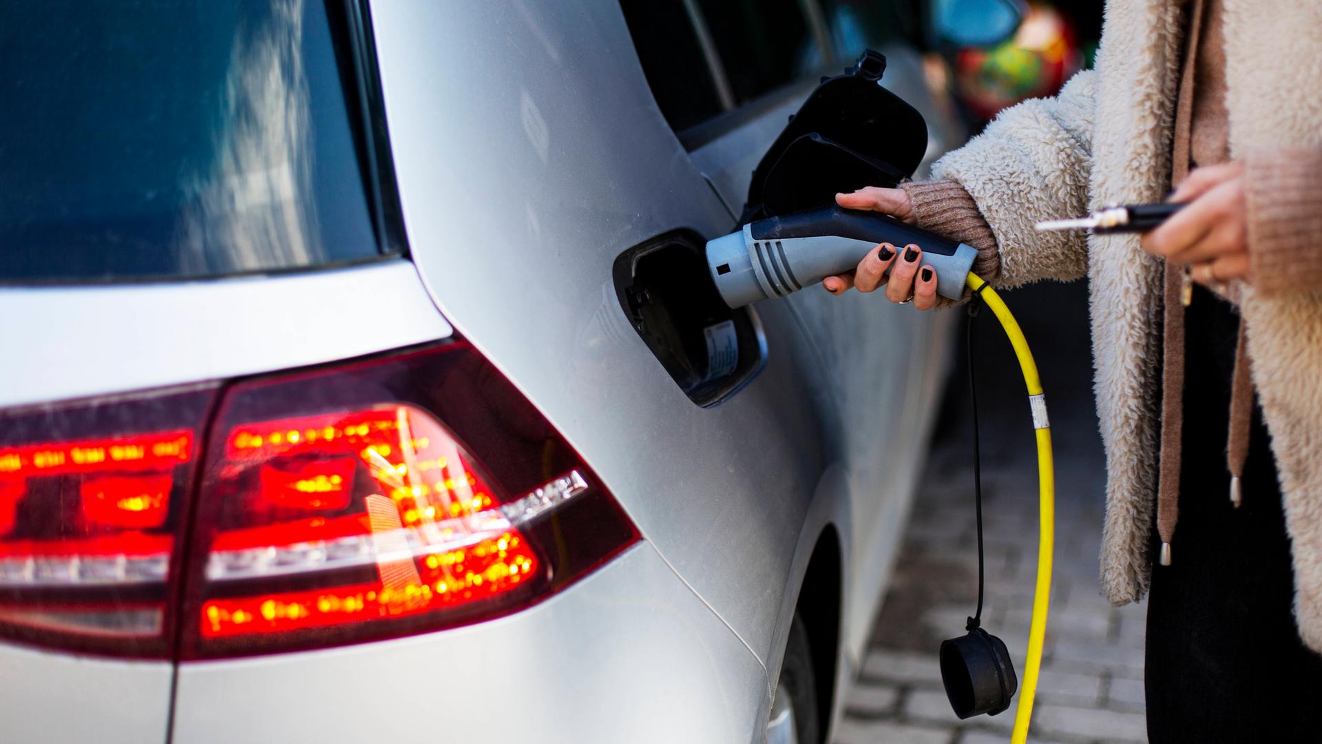 Eine Frau steckt den Ladestecker in ein E-Auto.